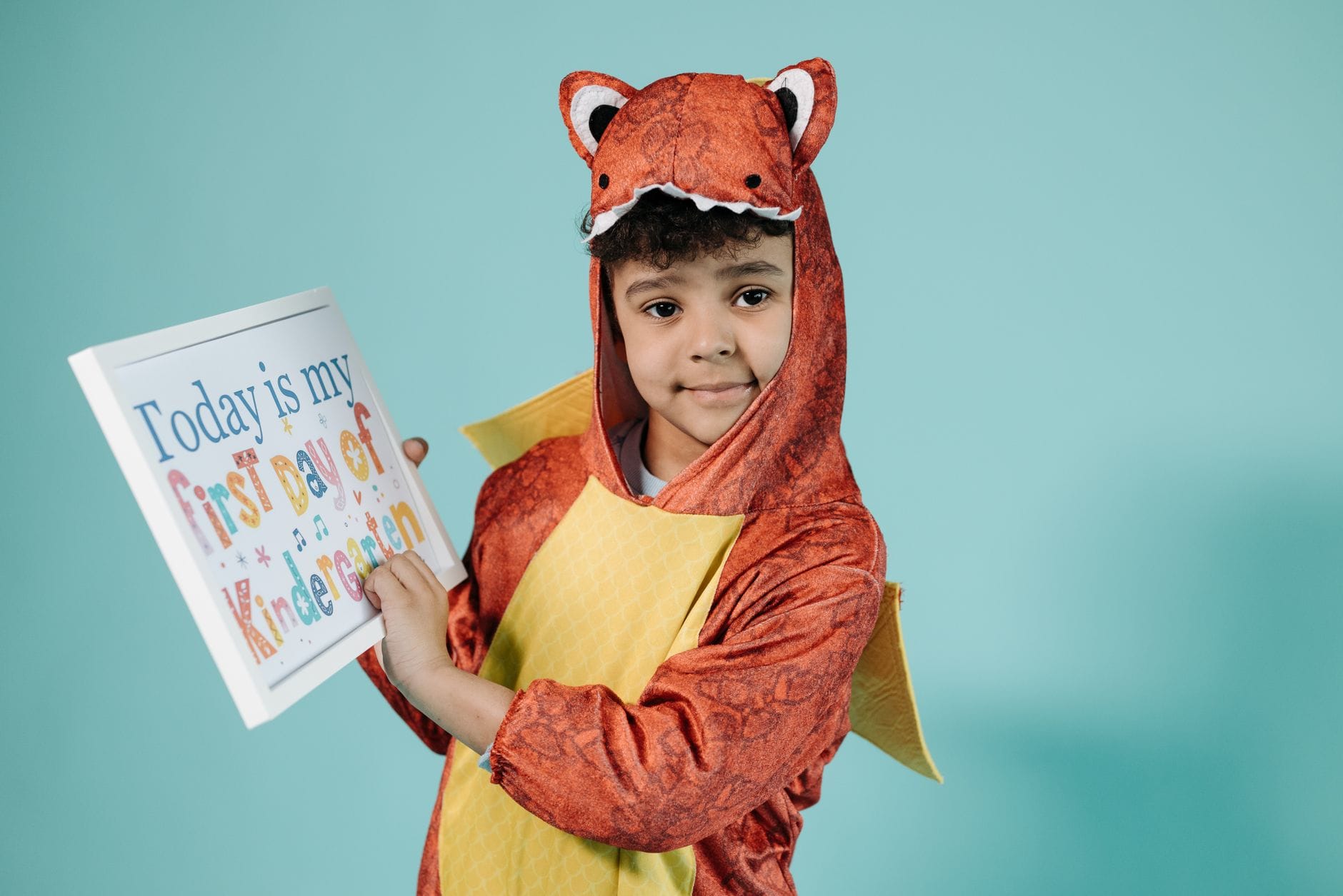 Dziecko w kostiumie dinozaura trzyma tabliczkę na pierwszy dzień przedszkola Dziecko w kostiumie dinozaura trzyma tabliczkę na pierwszy dzień przedszkola