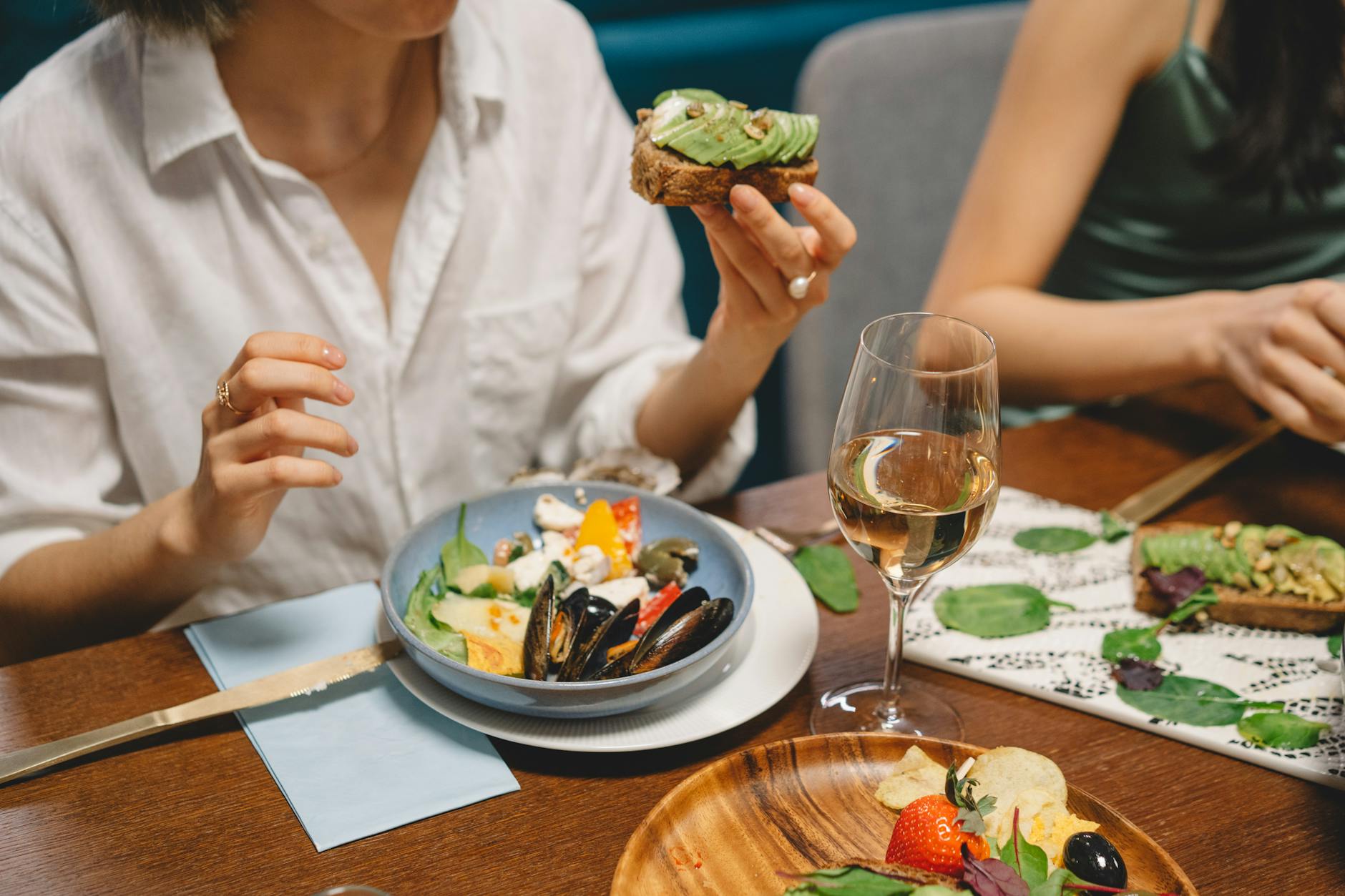 Przyjaciele jedzą awokado toast i owoce morza, popijając białe wino